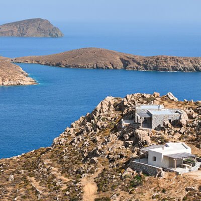 Masonry de pedra exposta transforma residência restaurada por c-o lab em harmonia com o terreno rochoso da ilha grega.